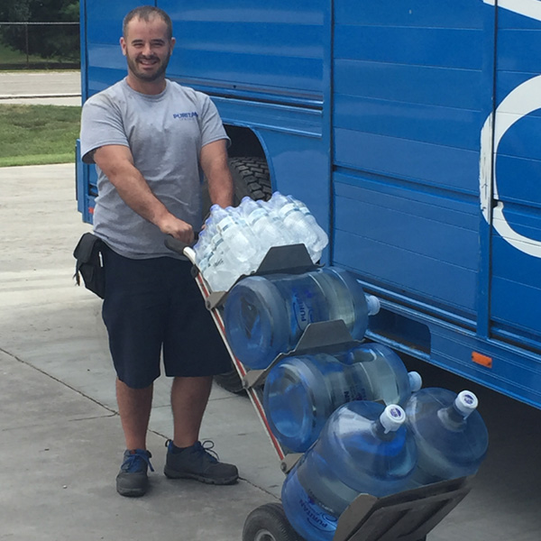 water delivery driver standing in front of truck, delivering 4 water cooler bottles and a case of water