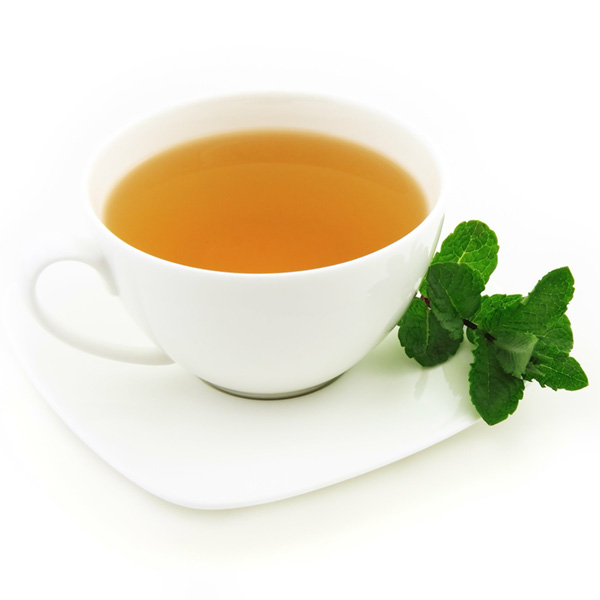 white teacup filled with tea, near a sprig of mint