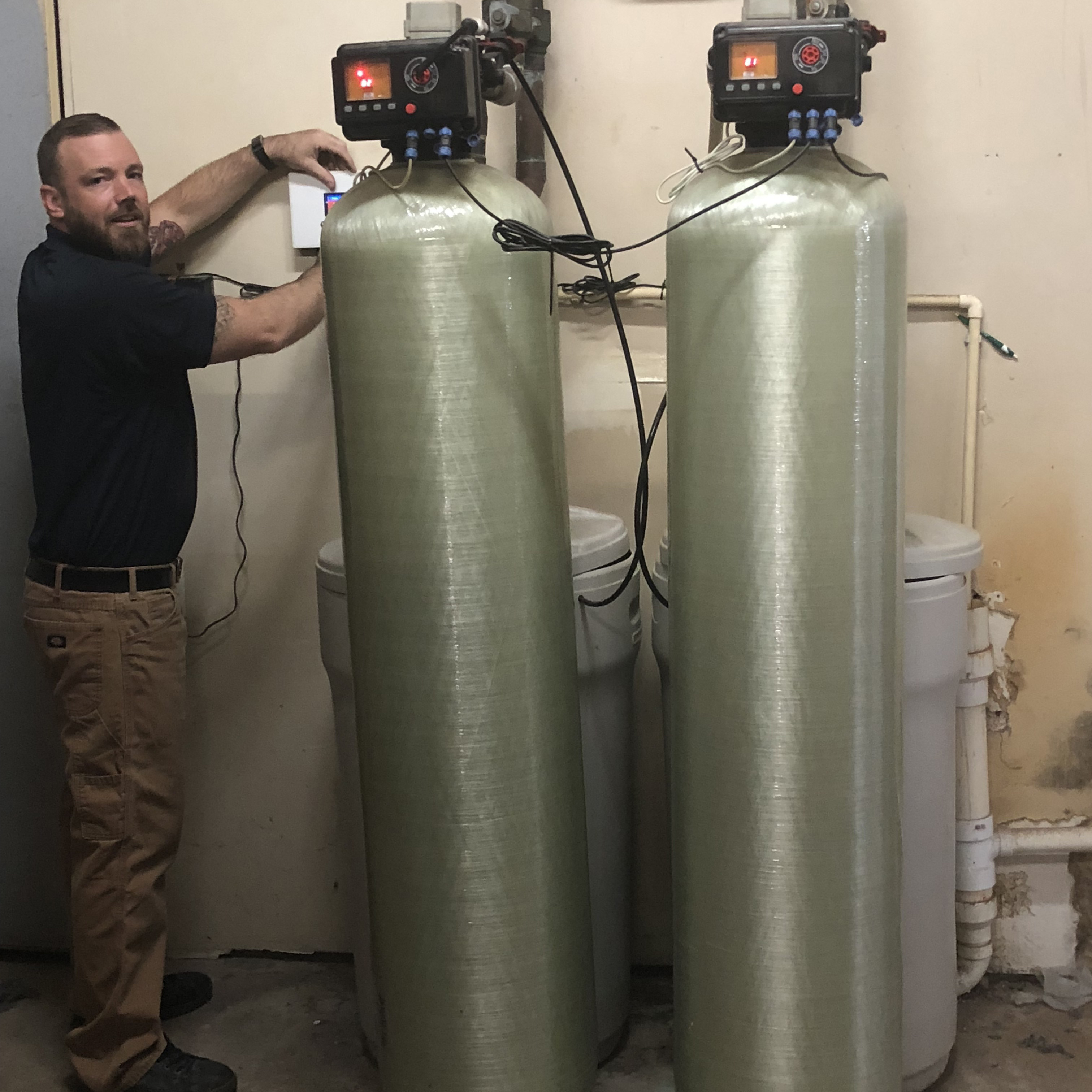 man installing two large, metal hard water filter tanks