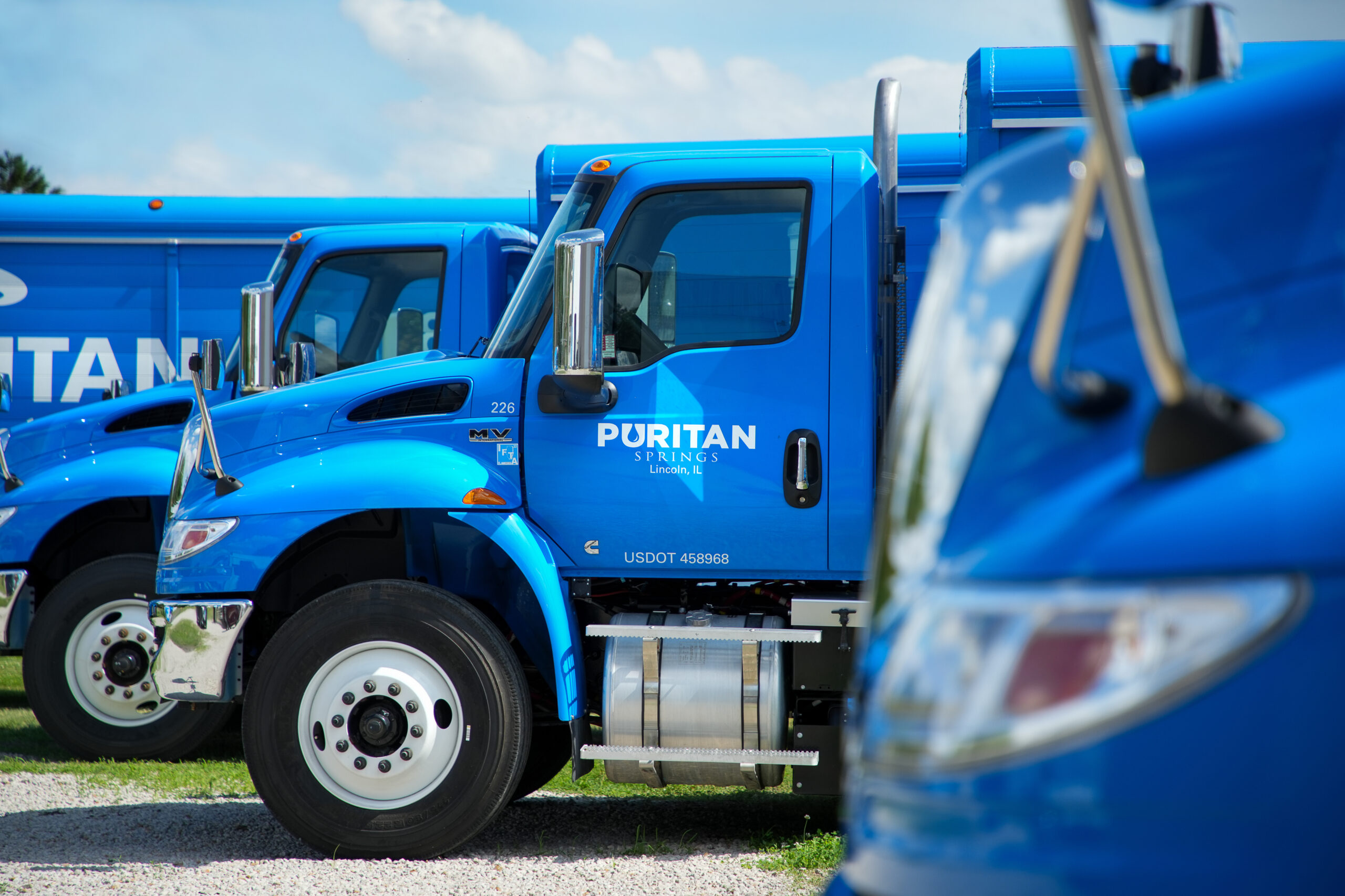 water delivery driver standing in front of truck, delivering 4 water cooler bottles and a case of water